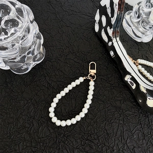 Detailed view of elegant white pearl phone strap with a golden lobster clasp on a dark fabric