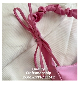 Detail of pink pleated shoulder bag with bow tie, metallic zipper, and textured fabric