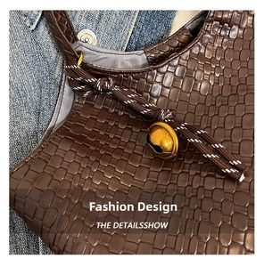 Close-up of brown woven leather shoulder bag with golden bell charm and rope detail