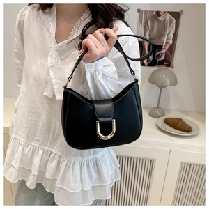 Close-up of minimalist black dumpling bag featuring a prominent gold D-shaped buckle
