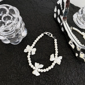 Detailed shot of white pearl phone strap featuring three elegant ribbon bow charms