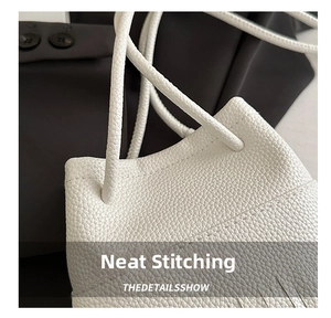 Macro detail of uniform stitching and lychee grain texture on a white shoulder bag