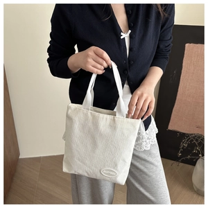 Detail of white corduroy tote bag showing striped texture and oval rubber brand label