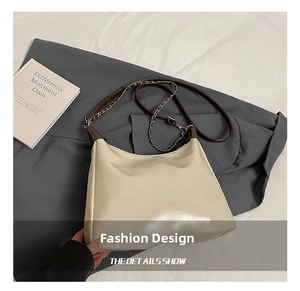 Detail view of cream tote bag featuring brown leather strap and silver chain accent