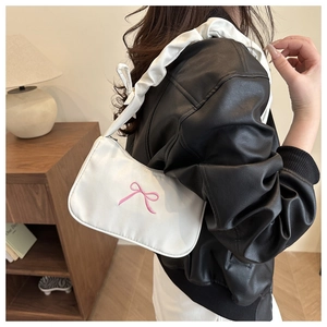 Detail of white underarm bag featuring pink bow embroidery and ruffled scrunchie strap