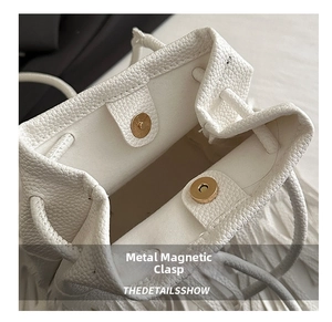 Detail of white bucket bag featuring lychee grain leather and a metal magnetic closure