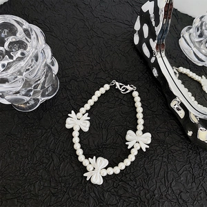 Detail view of pearl beaded phone strap with white bow accents on black textured background