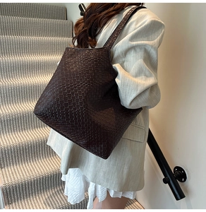 Détail d'un sac cabas en cuir tressé marron foncé montrant la texture et la bandoulière large