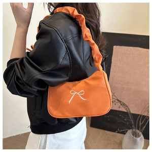 Détail du sac à bandoulière orange avec broderie nœud blanc sur tissu textile