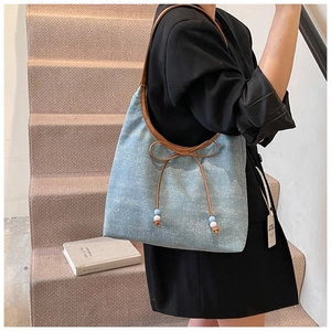 Detail of light blue denim tote with brown leather handles and bow bead charm