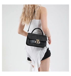 Detail view of black sequin crossbody bag with gold buckle on a white ruffled outfit