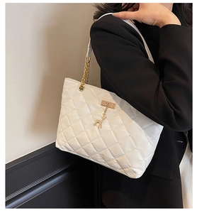 Detail of white quilted tote bag featuring golden deer charm and elegant chain strap