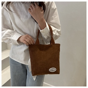 Detailed close-up of dark brown corduroy texture and brand logo leather patch on handbag