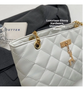 Detail of white quilted bag with golden chain and deer charm on grey fabric