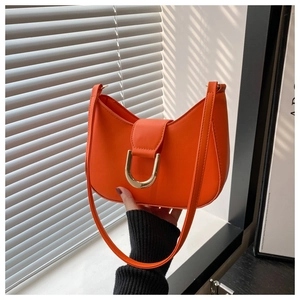 Close-up of vibrant orange crescent shoulder bag with bold gold U-shaped buckle detail