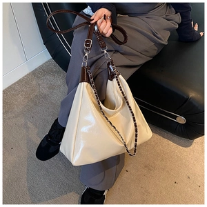 Detail of cream-colored glossy patent leather tote bag with brown handles and chain