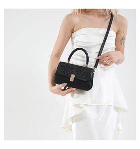 Detail view of a black vintage handbag with sequin flap and gold twist lock on a white dress