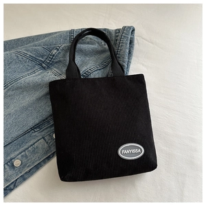 Close-up of black corduroy tote bag texture with small brand logo on white fabric