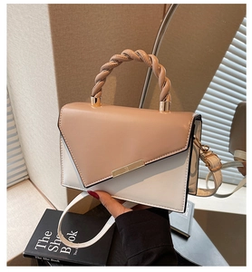 Dettaglio del manico in pelle intrecciata e hardware dorato sulla borsa a tracolla bicolore