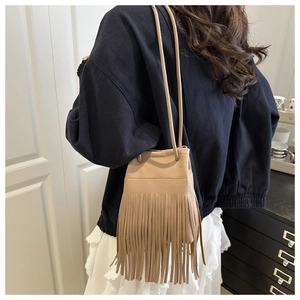 Chic beige tassel drawstring bucket bag shown worn as a crossbody by a model indoors