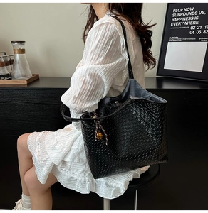 Détail d'un grand sac cabas noir tressé avec pendentif clochette dorée et bandoulière chic