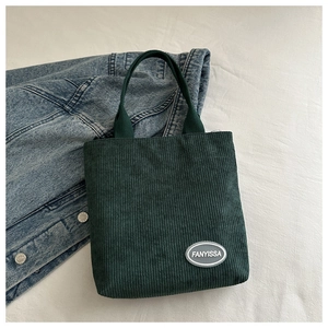 Detail of dark green corduroy tote bag showing vertical texture and logo patch