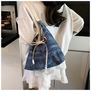 Detail of blue denim hobo bag with bow tie and beads, shown worn by a model in a kitchen