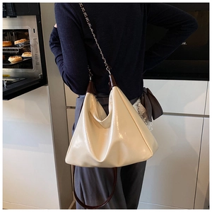 Close-up of off-white glossy pleated tote bag with chain strap worn by a model