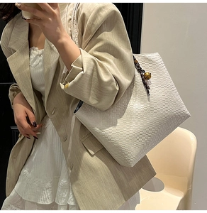 Gros plan sur le sac cabas tressé blanc avec poignées marron et breloque cloche dorée