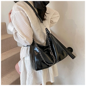 Detail of glossy black tote bag with silver chain strap worn with a white dress