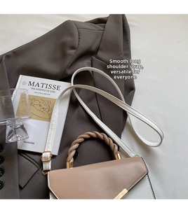 Dettaglio di una borsa bicolore in pelle con manico intrecciato marrone e chiusura oro