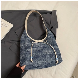Detail der dunkelblauen Denim-Achseltasche mit cremefarbener Schleife und Perlenakzenten