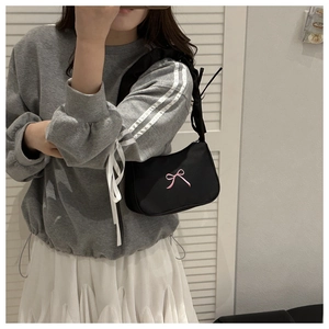 Close-up of black underarm bag featuring delicate pink ribbon bow embroidery and pleated strap