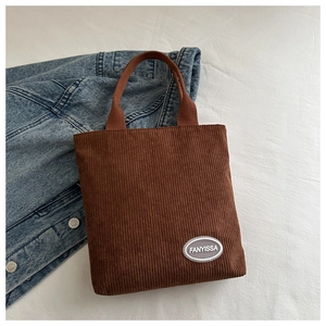 Detail of brown corduroy tote bag with vertical stripes and brand logo patch