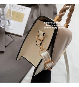Dettaglio degli anelli a D dorati e manico intrecciato sulla borsa beige