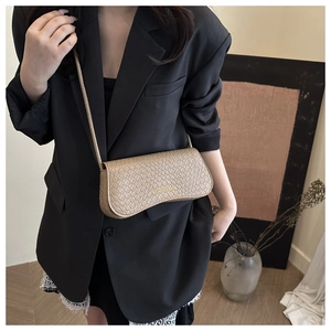 Detail of a textured cream baguette bag with logo on a black blazer-clad model