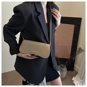 Close-up of beige woven baguette bag with adjustable strap worn on a black blazer