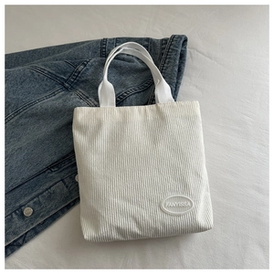 Detail shot of white corduroy tote bag featuring vertical stripe texture and brand label