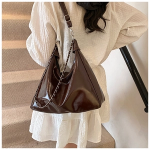 Deep brown glossy patent leather hobo bag with metal chain detail shown on a model's shoulder