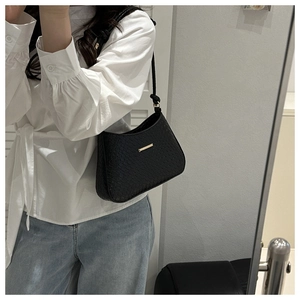 Detail of black faux crocodile leather shoulder bag featuring a sleek gold metal bar accent