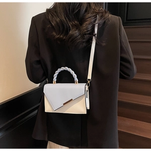 Détail du sac bandoulière bicolore avec poignée tissée porté sur un tailleur noir