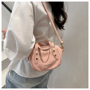 Detail view of a light pink leather bucket bag with gold rivets and adjustable shoulder strap