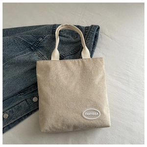 Detailed close-up of beige corduroy tote bag featuring a branded rubber patch and woven handle