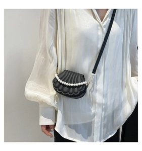 Détail d'un sac bandoulière coquillage noir avec perles sur une blouse blanche