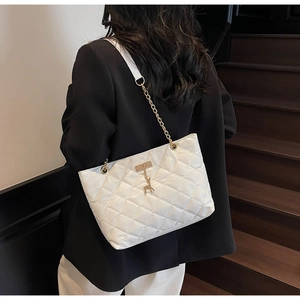 White quilted tote bag with golden chain and deer charm worn by a model in a black suit