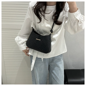 Detail of black woven crossbody bag featuring a golden buckle and knotted strap design