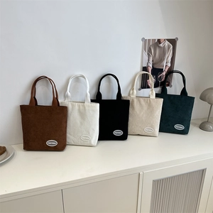 Five minimalist corduroy tote bags in various colors displayed on a white shelf