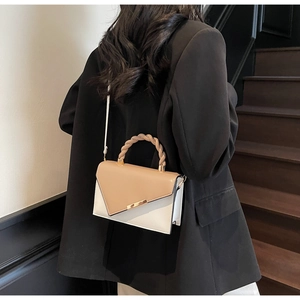 Détail d'un sac bandoulière bicolore avec poignée tressée porté par un mannequin de profil