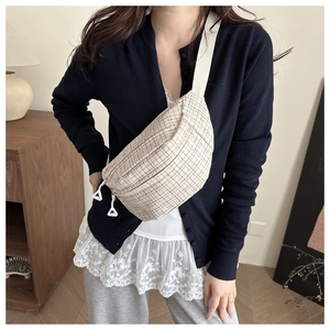Detail shot of cream tweed plaid chest bag with wide canvas strap on model in cozy interior