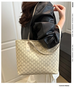 Detail of beige tote bag with M letter print and fashion plaque on model arm